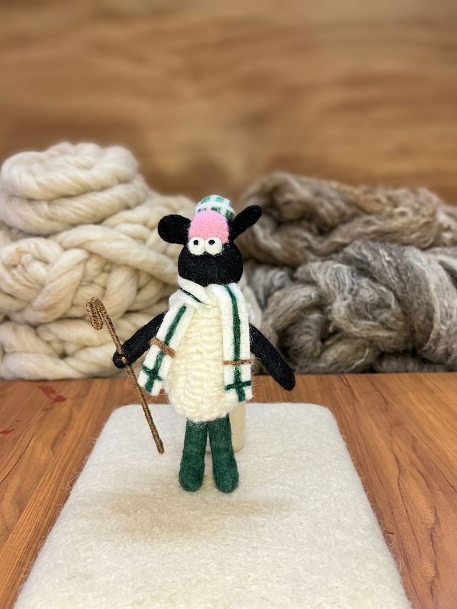 Felt sheep with a green scarf among wool skeins