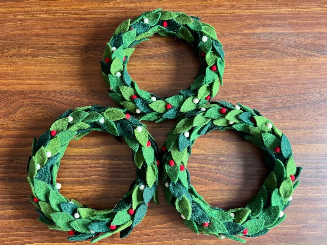 Three green felt leaf wreaths on a wooden table