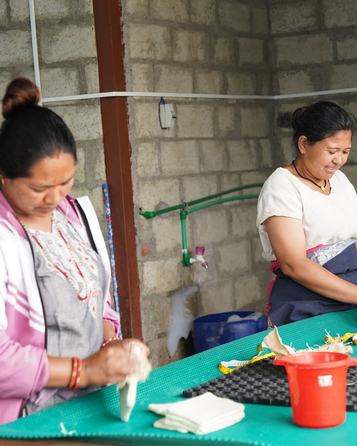 Two artisans finishing felt products at a workbench